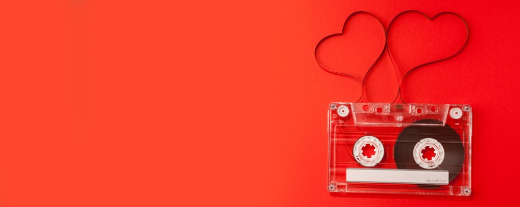 A clear music cassette over a read background. The tape has been pulled out to shape two hearts.